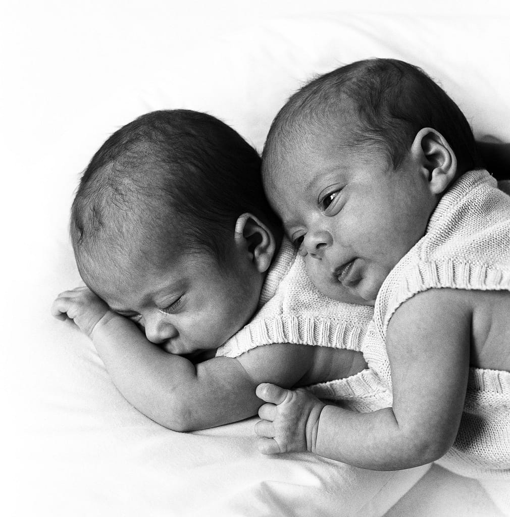 Zwillinge auf dem Bauch liegend, ein Zwillingsbaby hebt den Kopf und schaut beim Baby Fotoshooting in Hamburg Neustadt