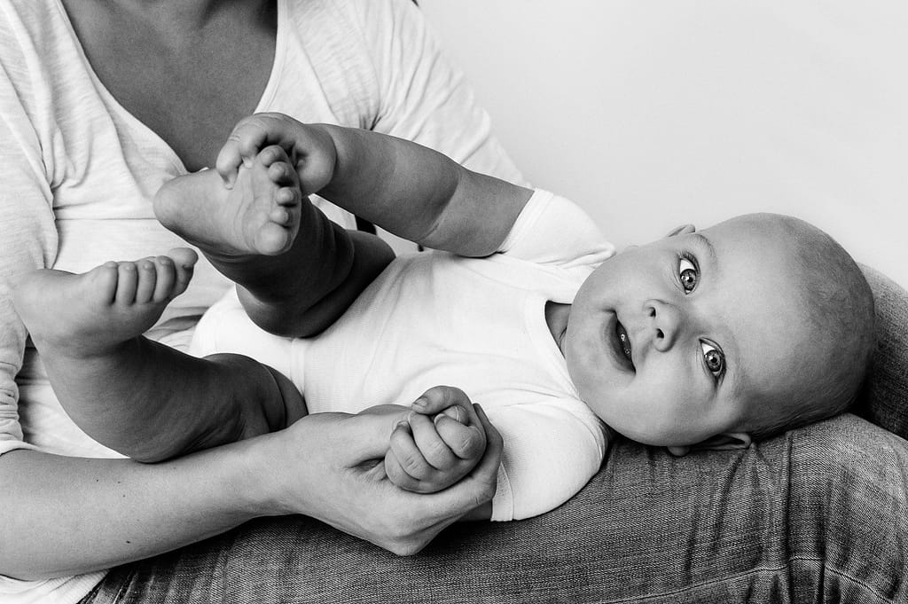 Baby liegt im Schoss seiner Mutter und greift nach seinen Füssen beim Baby Fotoshooting in Hamburg Eppendorf
