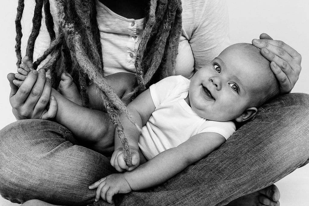 Baby liegt im Schoss seiner Mutter und spielt mit den Rastazöpfen beim Baby Fotoshooting in Hamburg Eppendorf