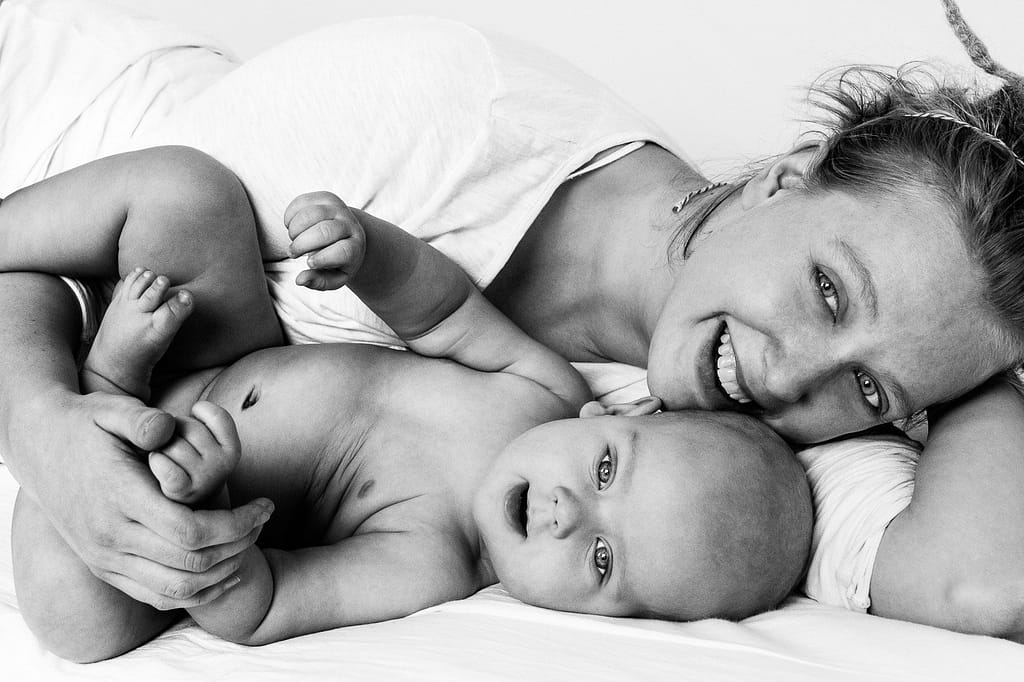 Mama und Baby liegen auf dem Bett und schmusen miteinander beim Baby Fotoshooting in Hamburg Eppendorf
