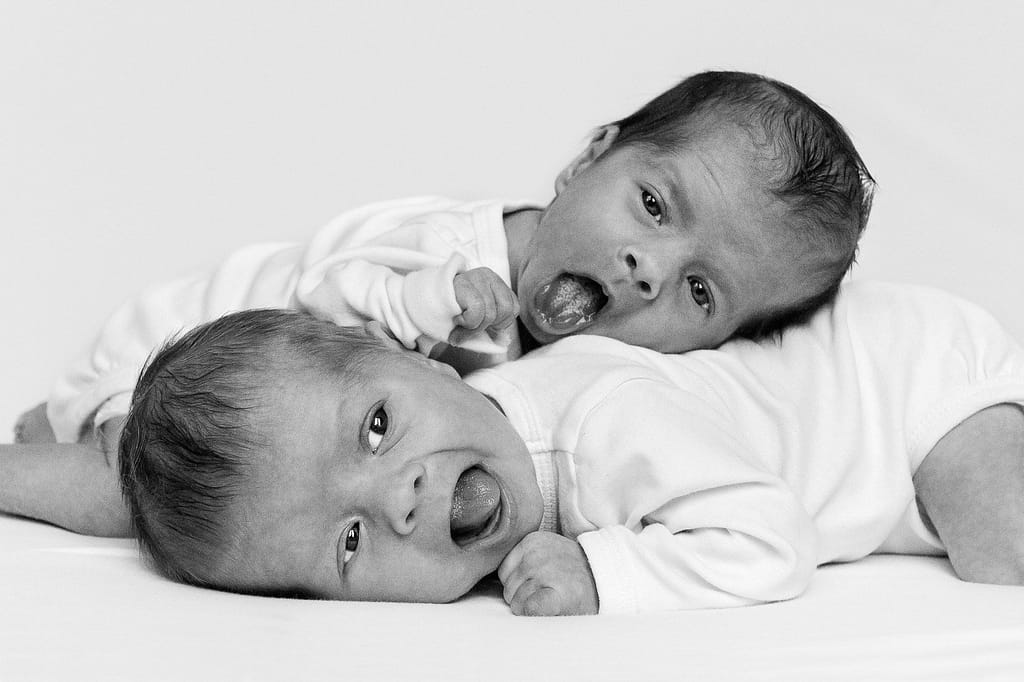 Zwillinge auf dem Bauch liegend und Zunge zeigend beim Baby Fotoshooting in Hamburg Barmbek