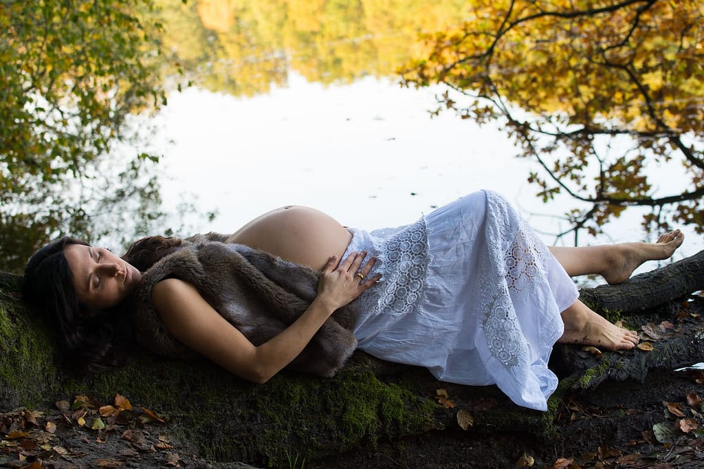 Schwangere liegt am Seeufer mit ihren Händen auf dem Babybauch beim Babybauch Shooting in Hamburg in der Natur