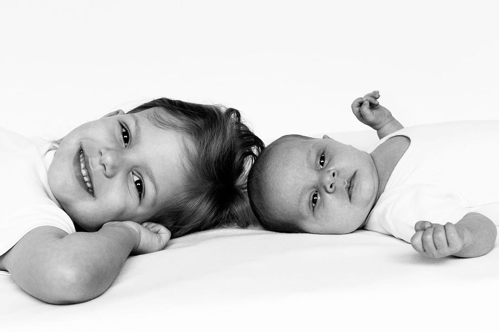 Baby und große kleine Schwester turnen gemeinsam auf der Tagesdecke beim Baby Fotoshooting zuhause in Hamburg Poppenbüttel