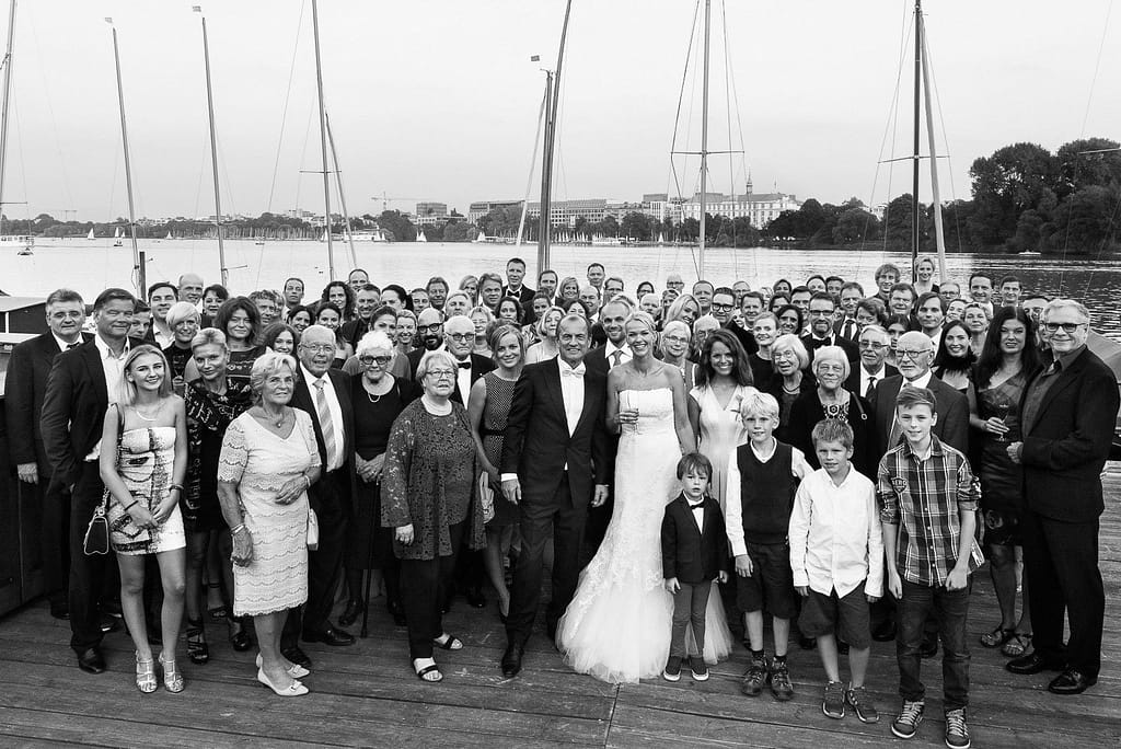 Gruppenbild der Hochzeitsgesellschaft auf dem Anleger vom Restaurante Portonovo mit Blick auf das Hotel Atlantic am Alsterufer auf der Außenalster am Rothenbaum beim Hochzeitsfotograf Hamburg