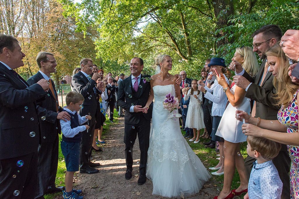 Das Hochzeitspaar läuft voller Freude an seinen Hochzeitsgästen vorbei, die spalier stehen und das Brautpaar in ein Meer aus Seifenblasen eindecken im Seelemannpark an der Eppendorfer Hochzeitskirche beim Hochzeitsfotograf Hamburg