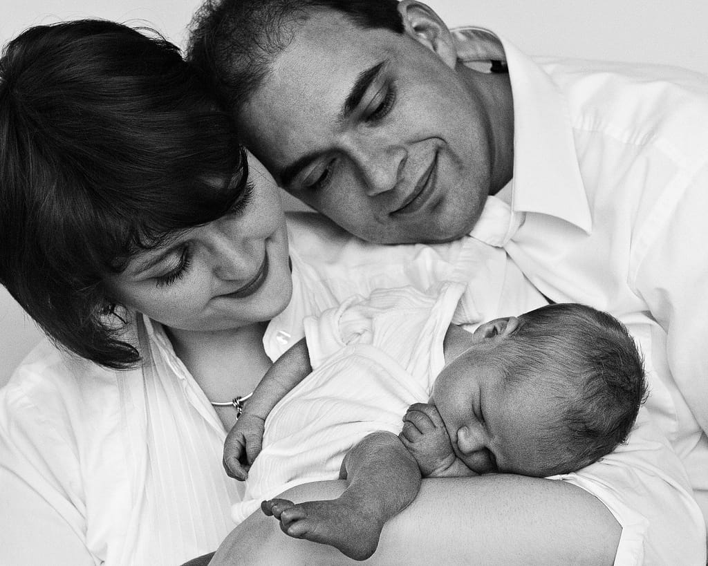 Mama und Papa halten ihr Baby im Arm und schauen es an bei der Neugeborenenfotografie in Hamburg Harburg