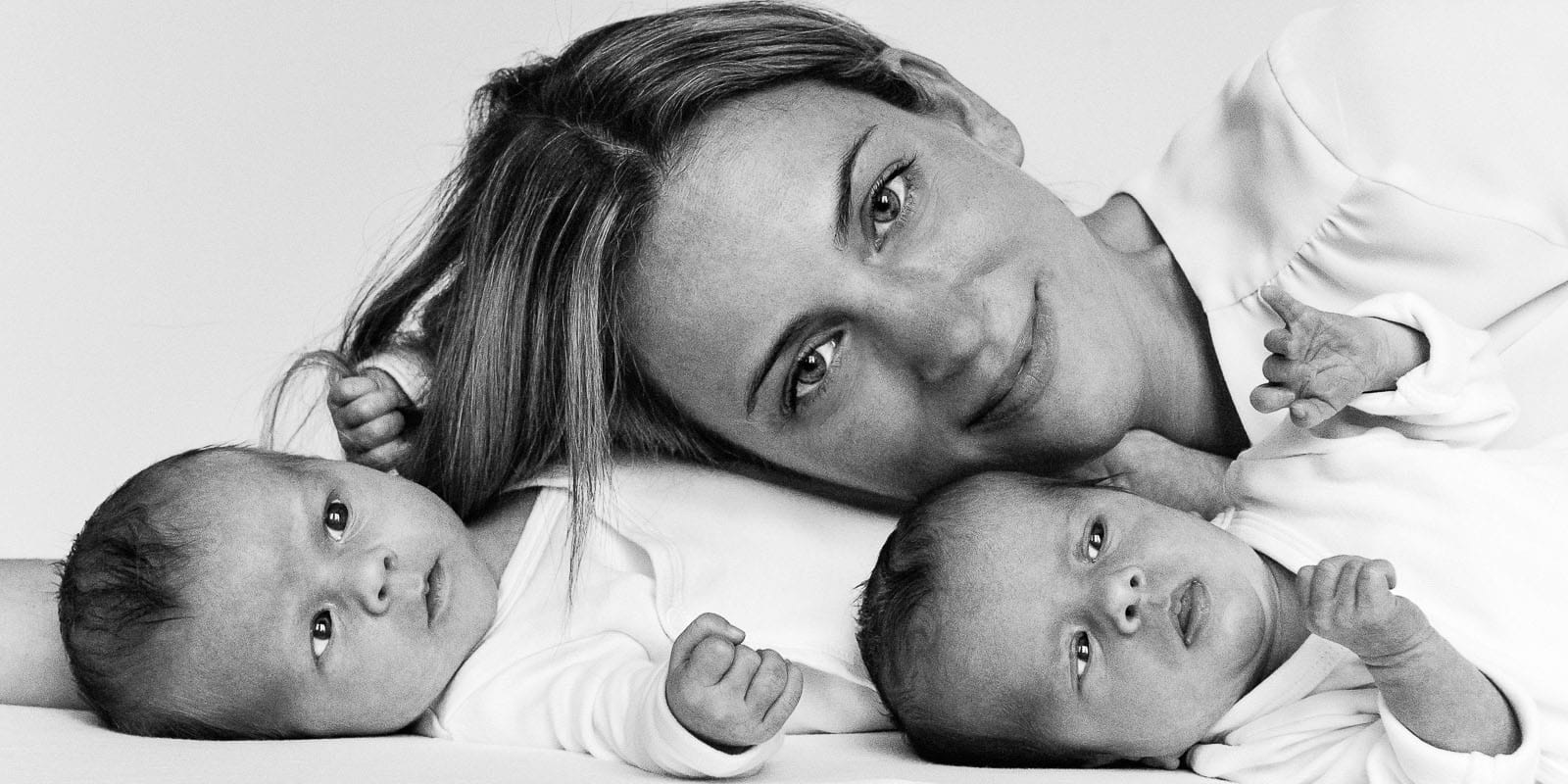 Mama und ihre Zwillinge liegen gemeinsam auf der Tagesdecke beim Baby Fotoshooting in Hamburg Barmbek