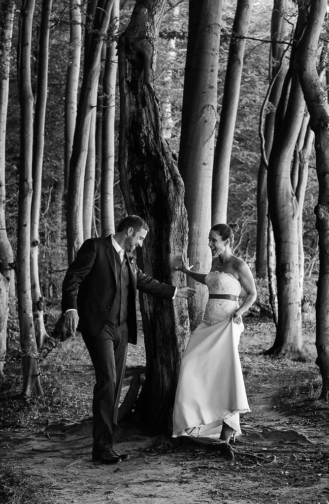 Braut und Bräutigam schlendern gemeinsam um die Bäume im märchenhaften Hochuferwald am Weissenhäuser Strand an der Ostsee beim Hochzeitsfotograf Hamburg
