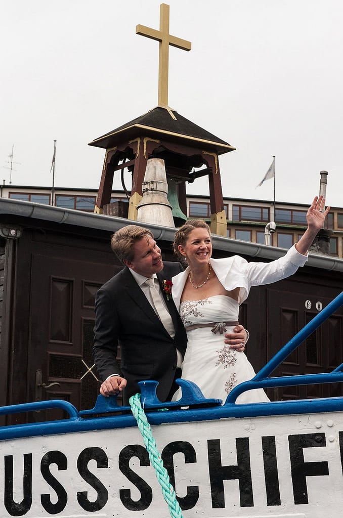 Das Hochzeitspaar winkt seinen Hochzeitsgästen von der Flußschifferkirche zu. Die Hochzeitsbilder vom Hochzeitsfotograf Hamburg
