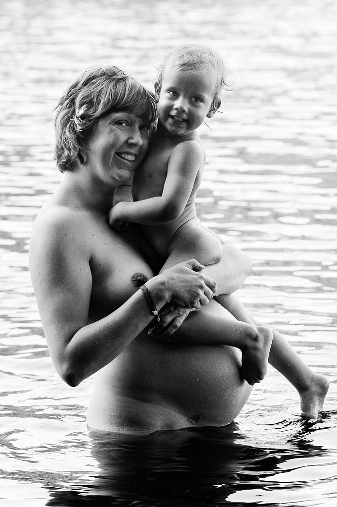 Mutter steht im Wasser mit ihrem Kind auf dem Arm beim Babybauch Shooting in Hamburg am See in der Natur