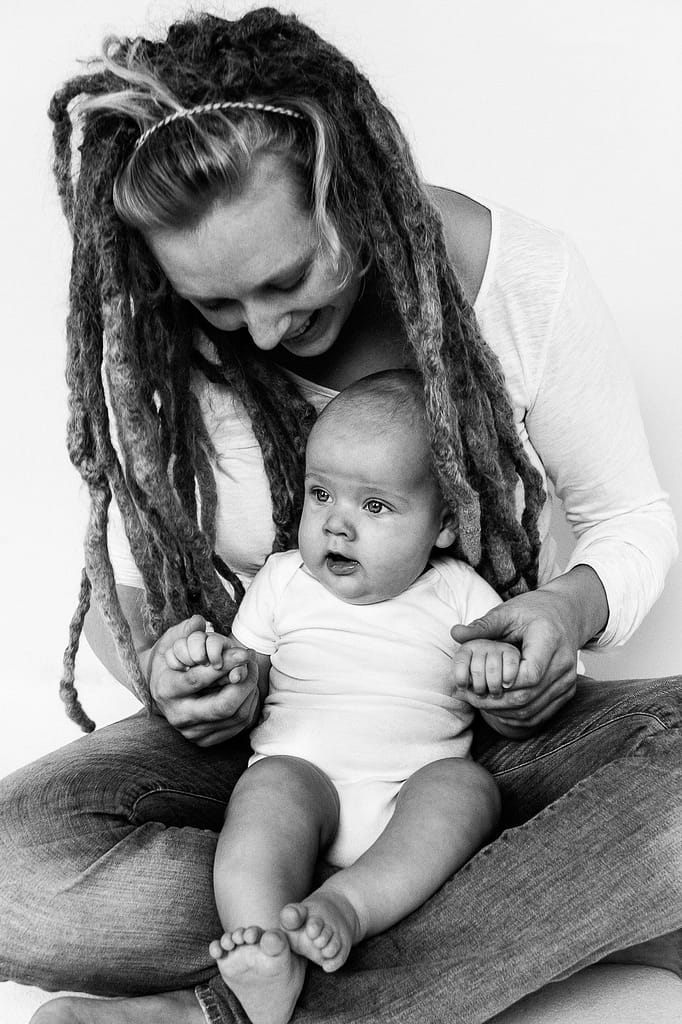Baby sitzt auf Mamas Schoss und wird an den Händen gehalten beim Baby Fotoshooting in Hamburg Eppendorf