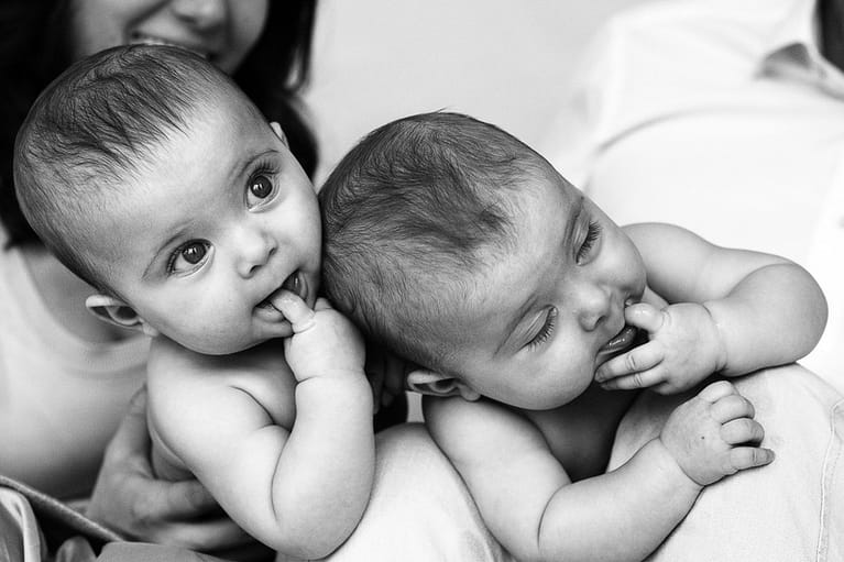 Zwillinge nebeneinander auf dem Bauch liegend mit dem Finger im Mund beim Baby Fotoshooting in Hamburg Rotherbaum