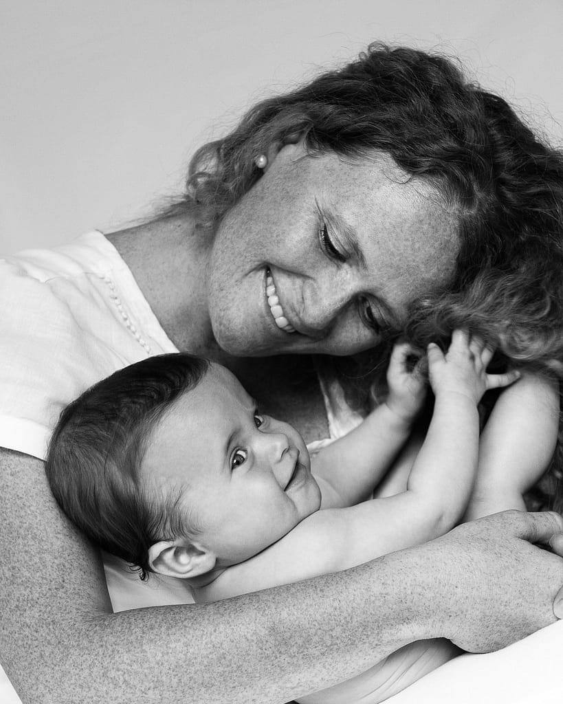 Mama hält Baby im Arm und Baby spielt mit den Haaren seiner Mutter beim Baby Fotoshooting in Reinbek bei Hamburg