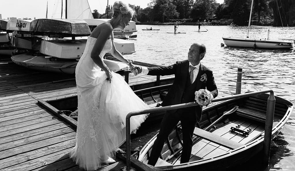 Der Bräutigam hilft seiner Braut in ein Rucerboot am Bobby Reich Bootsteg an der Außenalster in Harvestehude beim Hochzeitsfotograf Hamburg
