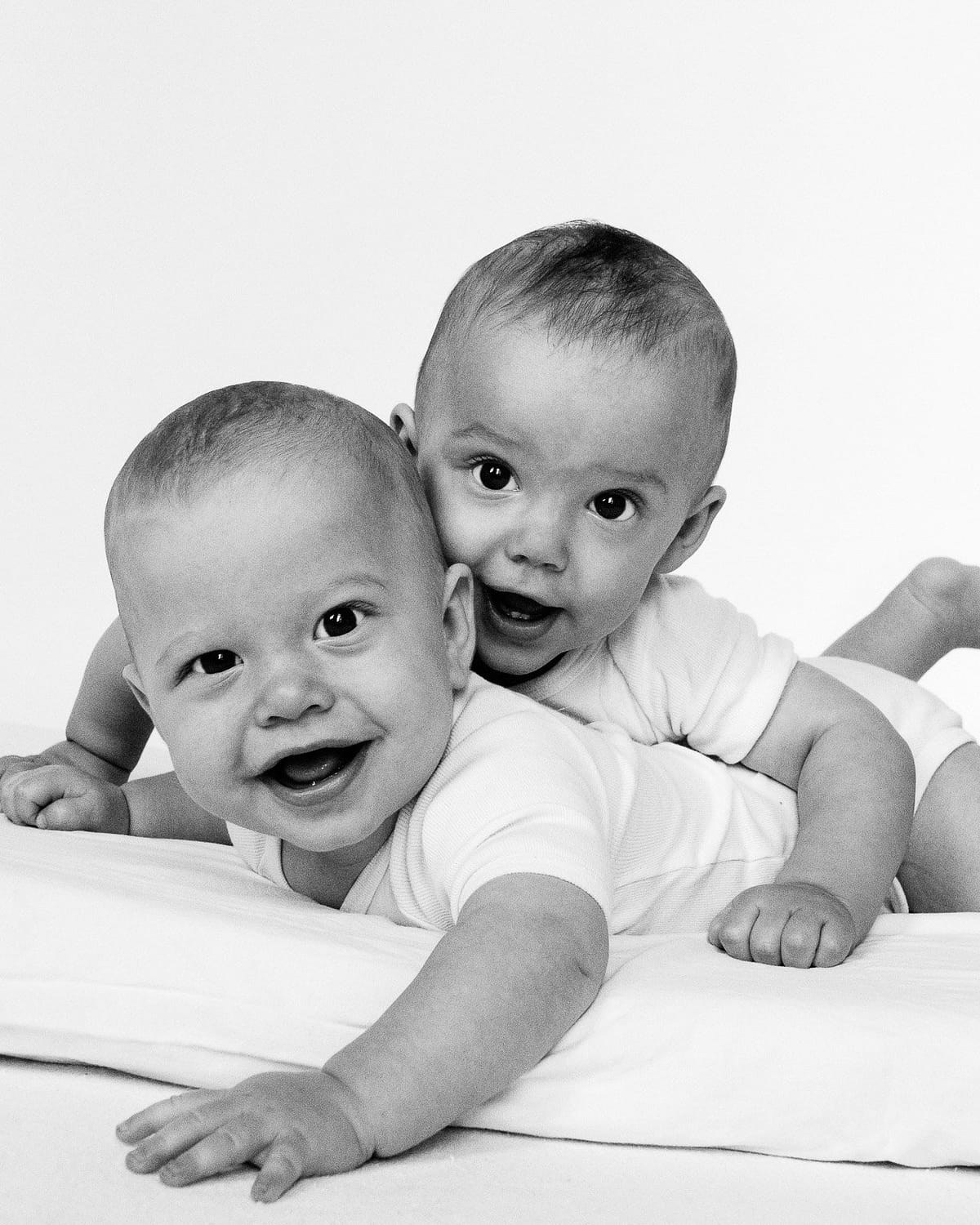 Zwillinge liegen nebeneinander auf dem Bauch und schauen auf beim Baby Fotoshooting in Hamburg Langenhorn