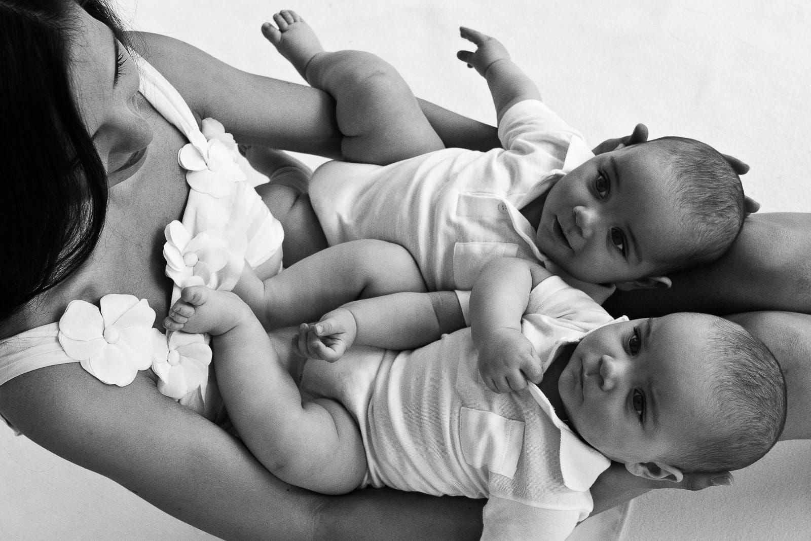 Mama hat beide Zwillinge nebeneinander auf ihren Beinen liegend und schaut sie an beim Babyfotograf in Hamburg Harvestehude