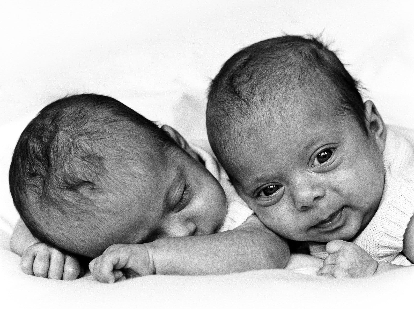 Zwillinge auf dem Bauch liegend, ein Zwillingsbaby hebt den Kopf und schaut beim Baby Fotoshooting in Hamburg Neustadt