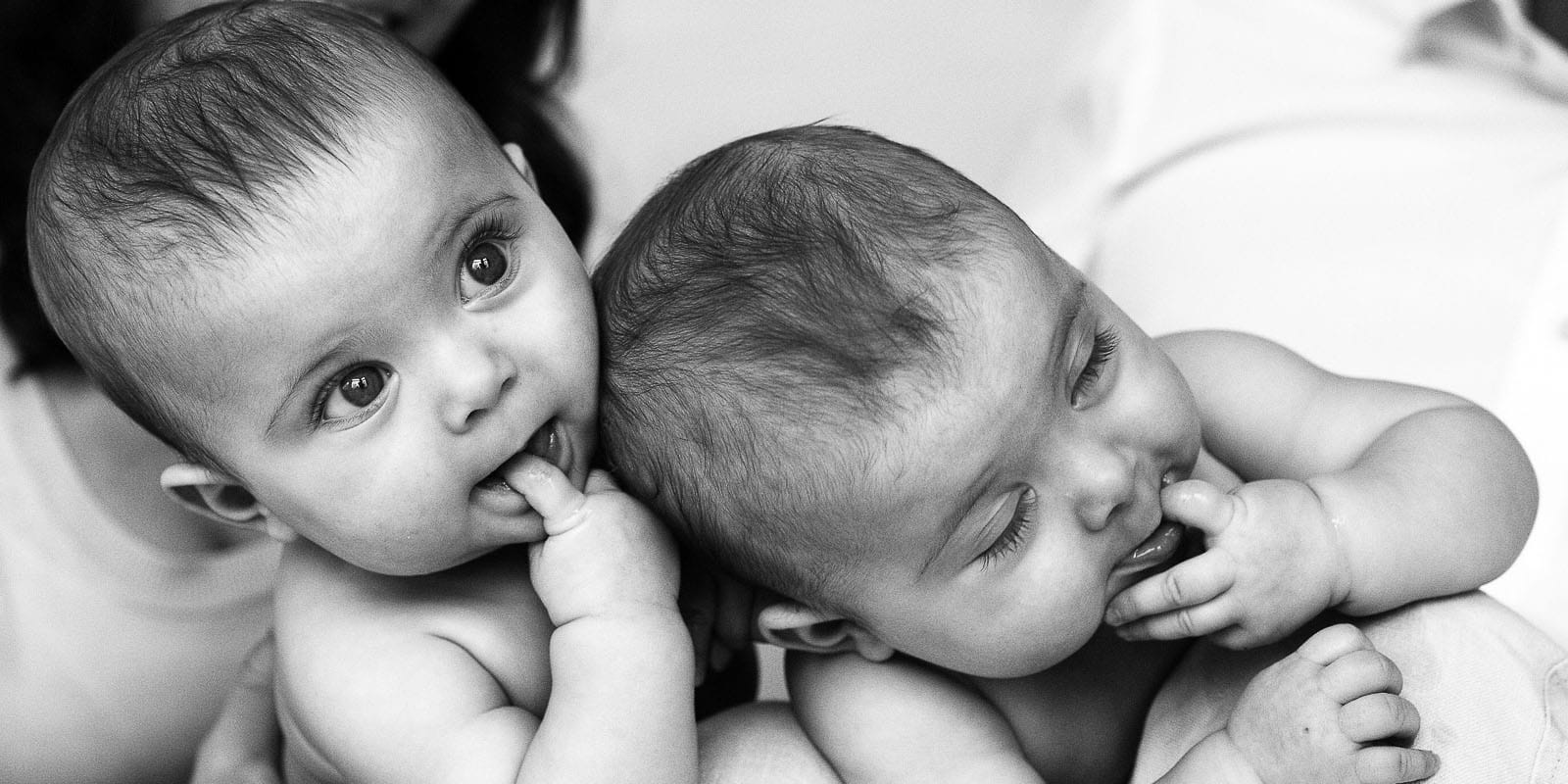 Zwillinge nebeneinander auf dem Bauch liegend mit dem Finger im Mund beim Baby Fotoshooting in Hamburg Rotherbaum