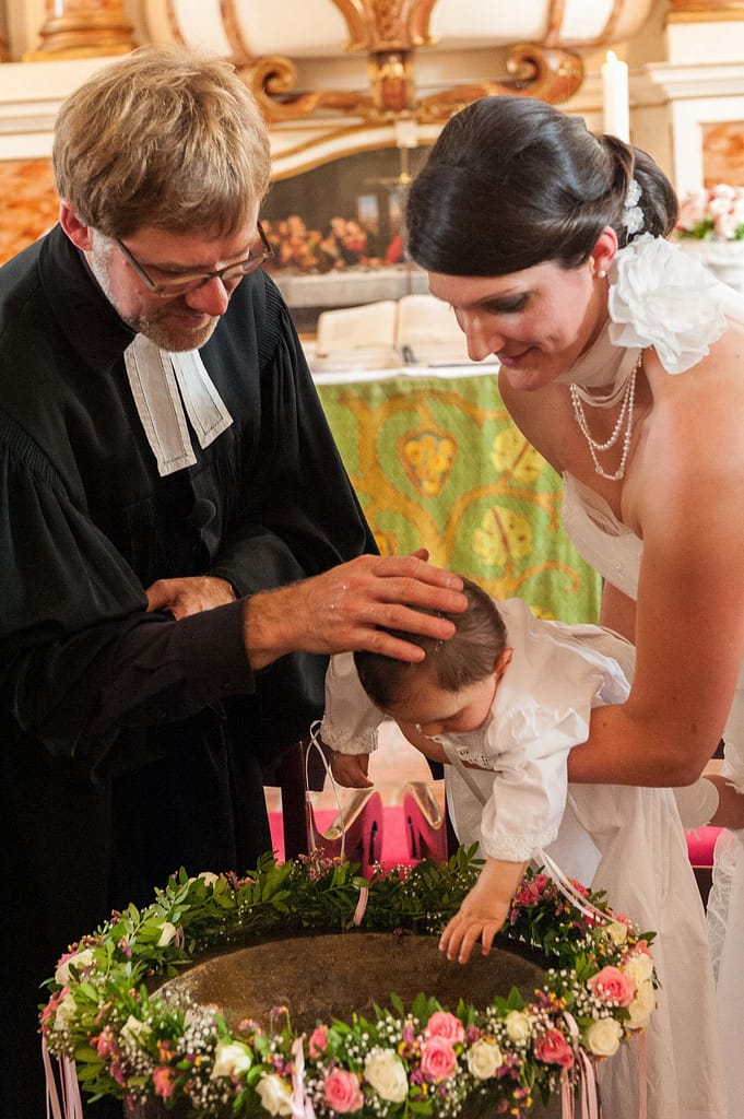 Bei der Taufe am Taufbecken erteilt der Pastor den Segen in der Hochzeitskirche in Nienstedten an der Elbe beim Hochzeitsfotograf Hamburg