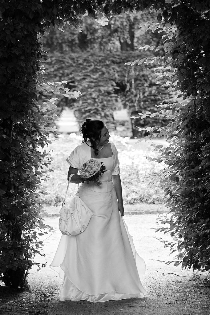 Die Braut hält Ausschau nach ihrem Bräutigam im Adam und Eva Heckengarten im Hamburger Stadtpark in Winterhude bei den Brautpaarfotos beim Hochzeitsfotograf Hamburg