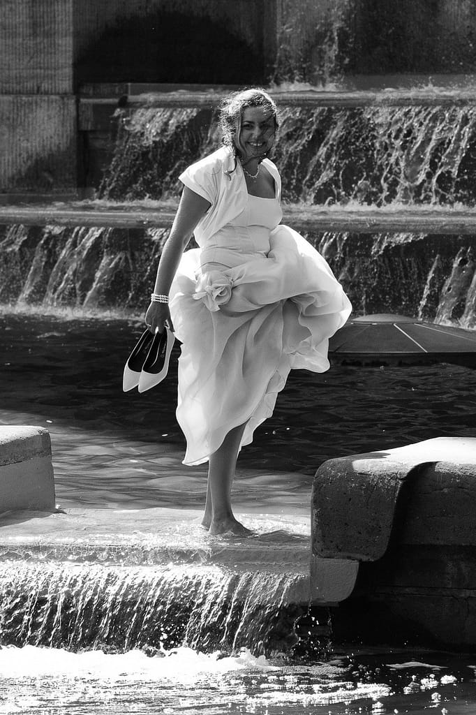 Braut im Brautkleid badet mit den Füssen im Springbrunnen vor dem Planetarium im Hamburger Stadtpark bei den Brautpaarfotos bei den Brautpaarfotos beim Hochzeitsfotograf Hamburg