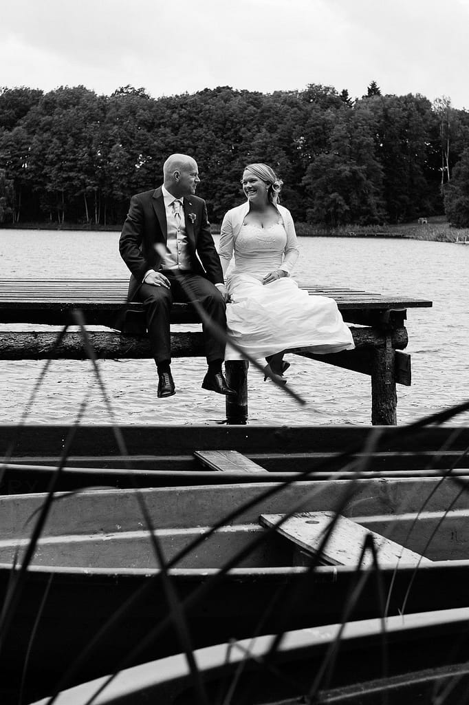Hochzeitspaar sitzt händchenhaltend auf dem Bootssteg bei der Landhochzeit am Tangahnsee bei Warlow am Gutshof Woldzegarten in Mecklenburg Vorpommern beim Hochzeitsfotograf Landhochzeit Hamburg