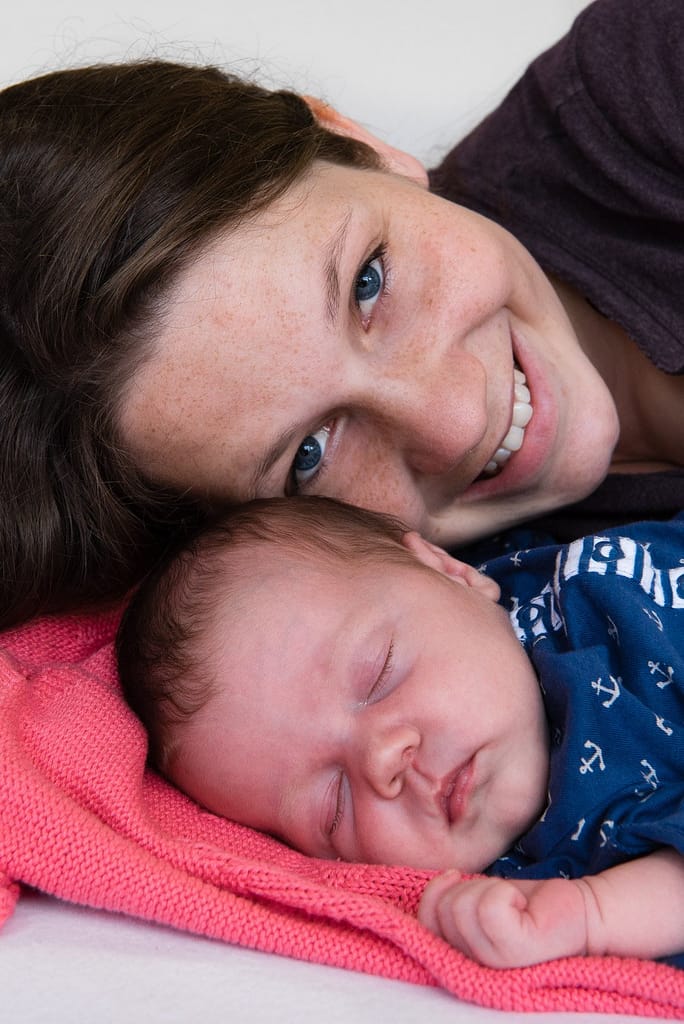 Mama kuschelt sich an ihr schlafendes Baby und freut sich beim Baby Fotoshooting in Hamburg Osdorf