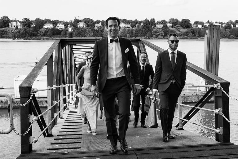 Der Bräutigam führt seine Hochzeitsgäste vom Anleger Bubendeyufer an der Elbe zur Villa im Jachthafen bei Hochzeitsfotografie Hamburg