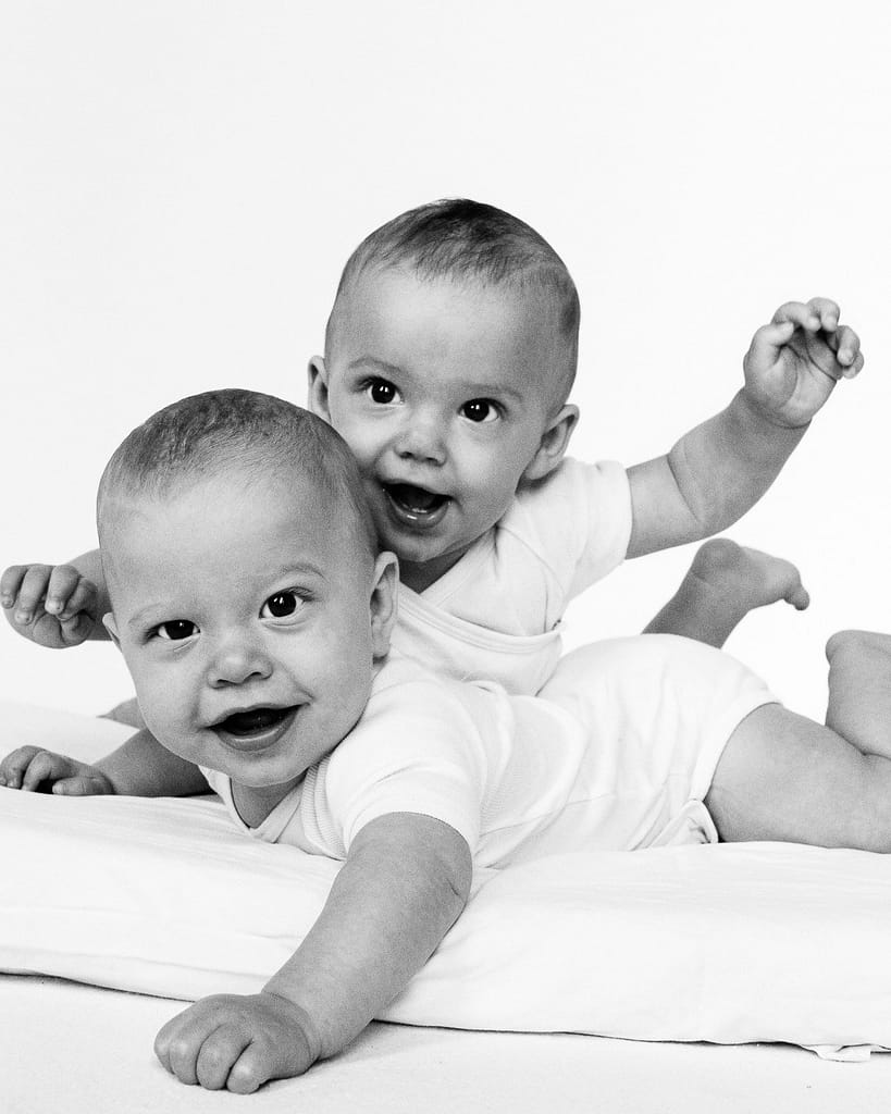 Zwillinge liegen nebeneinander auf dem Bauch und schauen auf beim Baby Fotoshooting in Hamburg Langenhorn